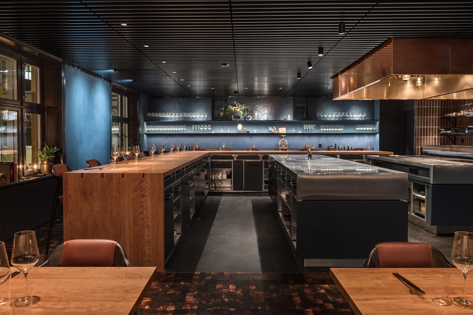 Refined restaurant open kitchen with stainless equipment, copper ventilation and dark cabinetry